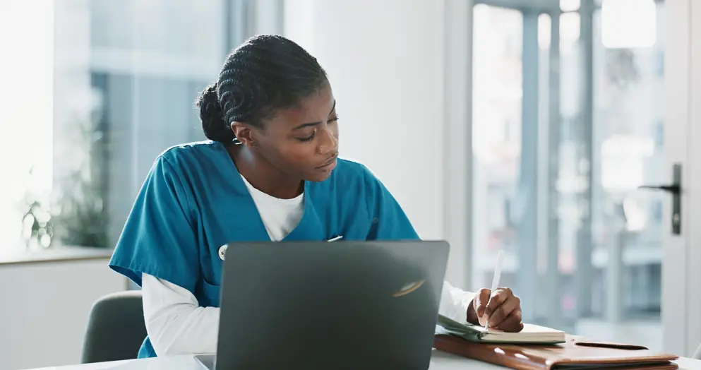 Female doctor making notes from information she is looking at on a laptop. 