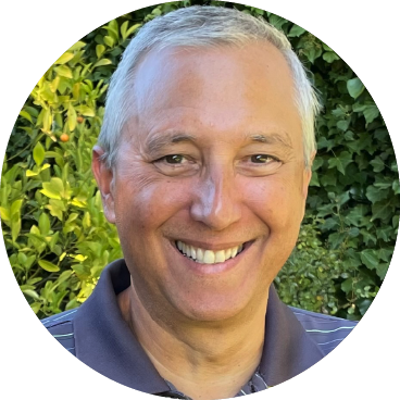 Douglas Cappiello smiling outdoors in front of green foliage.